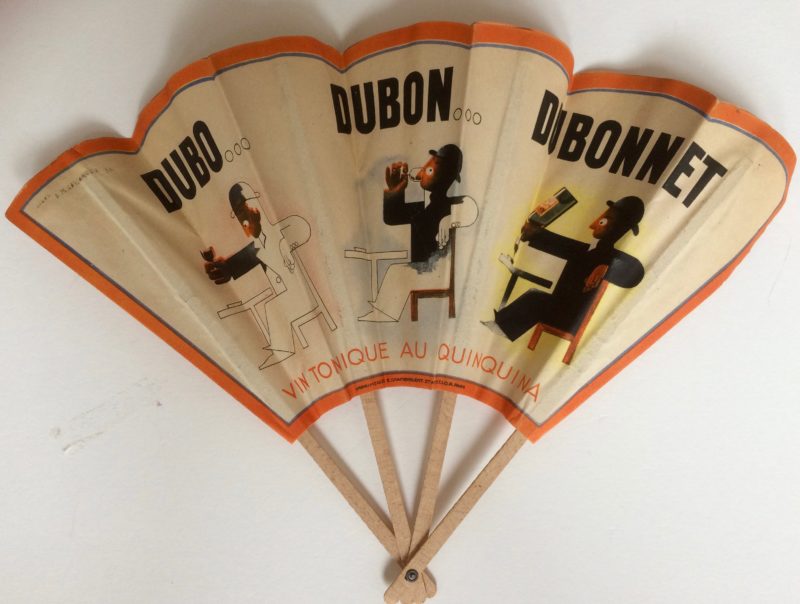 A vintage fan with an image of 3 versions of the same man drinking at a table printed on it